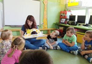 Dzieci słuchają i oglądają książkę "Kolorowy potwór"